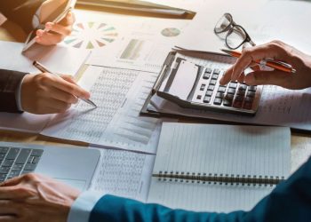 Two colleauges working through the annual accounts using a lot of paper receipts, charts, a laptop and calculators
