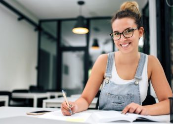 A female student entrepreneur sitting at a desk of the University computer room working on a student business and also studying