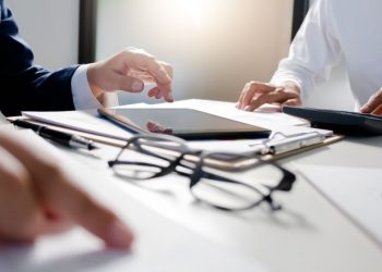 An accountant and business owner discussing capital tax gains allowances and calculations surrounded by documents, computers and calculators