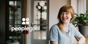 An image of a woman smiling in an office looking at the People Goal logo