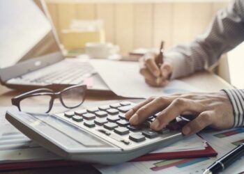 Small business owner doing annual accounts using accounting software, calculator and paper pads