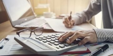 Small business owner doing annual accounts using accounting software, calculator and paper pads