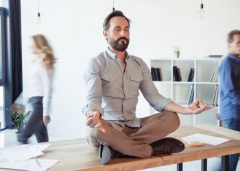 Sitting on a desk a businessman is mediating in the middle of the work day to recover focus