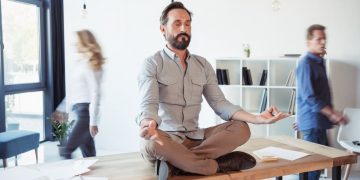 Sitting on a desk a businessman is mediating in the middle of the work day to recover focus