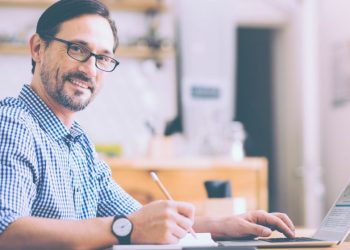 Entrepreneur sitting a desk smiling while he carries out the daily work of running a business
