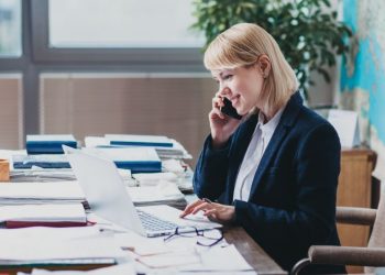 Senior director at a PR firm at her desk purusuing papers on the phone with a client discussing public relations