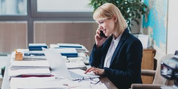 Senior director at a PR firm at her desk purusuing papers on the phone with a client discussing public relations