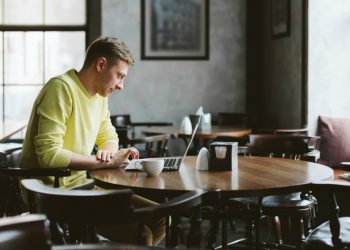 Man working out a pub with a cup of coffee next to him while he remote works