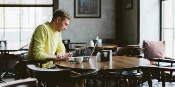 Man working out a pub with a cup of coffee next to him while he remote works