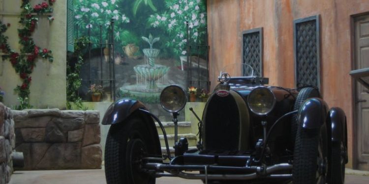 A vintage car from the early 20th century set against the backdrop of a stone courtyard