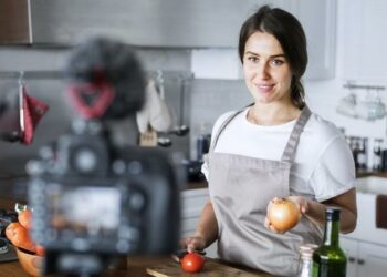A female vlogger standing infront off a camera demonstrating how to cook (an example of influencer marketing)