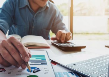 A business person assessing the different types of financing by using a laptop and paperwork to research