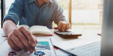 A business person assessing the different types of financing by using a laptop and paperwork to research