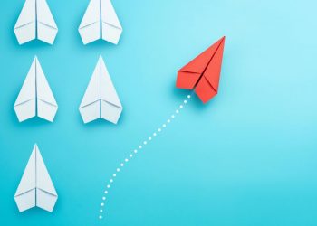 A series of white paper aeroplanes with one plane in red deviating symbolising how sometimes contray business advice is the best advice