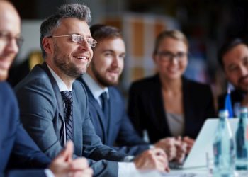 A smiling man in a suit in a group of fellow employees exampling him as the best employee recruited