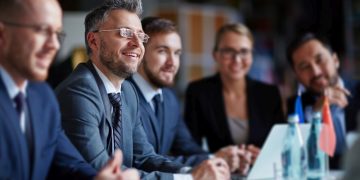 A smiling man in a suit in a group of fellow employees exampling him as the best employee recruited
