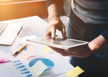 business man holding  digital tablet and use laptop to working document accountant analyze income & budget & tax is are planning a marketing plan to improve the quality of their sales in the future.