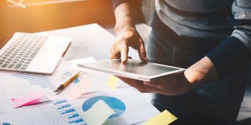 business man holding  digital tablet and use laptop to working document accountant analyze income & budget & tax is are planning a marketing plan to improve the quality of their sales in the future.