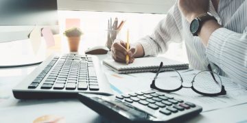A entrepreneur using a computer, calculator and paper to work out how he can better budget