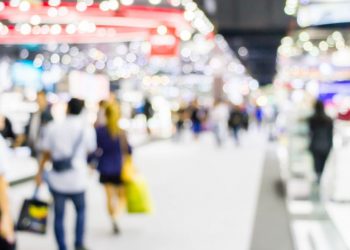 An image of a tradeshow with blurred business people walking around exploring vendor kiosks