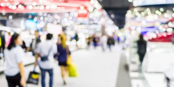 An image of a tradeshow with blurred business people walking around exploring vendor kiosks