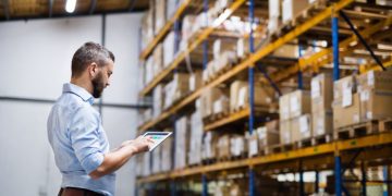 A warehouse manager checking stock levels via iPad in a warehouse