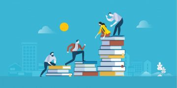 A team of learning management system employees working together to help each other climb a set of books, a metaphor for working together to achieve an LMS marketing strategy