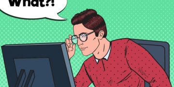 A man staring at a computer screen, adjusting his glasses to try and see the screen