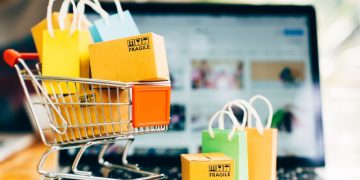 A mini shopping trolley filled with packages in front of a laptop open on an eCommerce website, symbolsing how having the right eCommerce theme can make a difference to sales