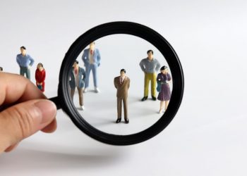 A magnifying glass focusin in on a model person in a crowd, as a metaphor for finding local talent