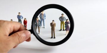 A magnifying glass focusin in on a model person in a crowd, as a metaphor for finding local talent