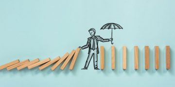 A person stopping a series of dominoes toppling any further, as a metaphorical example of how business interruption insurance can save businesses from being completely destroyed