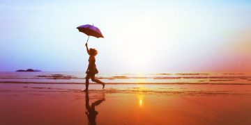 A person running along the beach with an umbrella on a sunny day, symbolising preparing for the worst as life insurance does