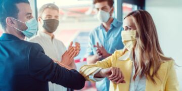 Business people wearing face masks and bumping elbows during COVID to signify closing a sales deal