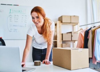 Female entrepreneur working on a laptop next to a product she's about to ship to a customer from her eCommerce store