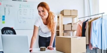 Female entrepreneur working on a laptop next to a product she's about to ship to a customer from her eCommerce store