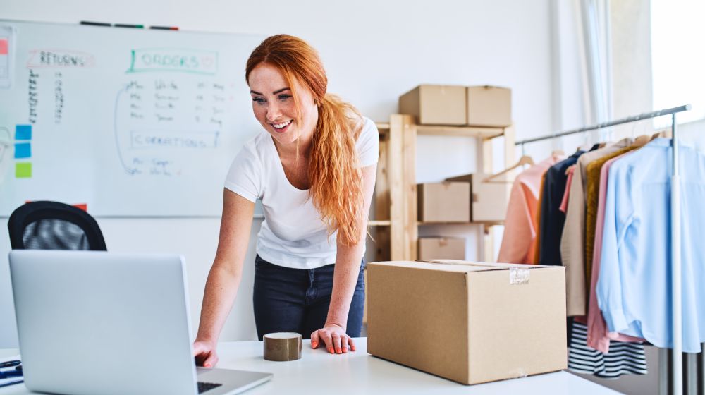 Female entrepreneur working on a laptop next to a product she's about to ship to a customer from her eCommerce store