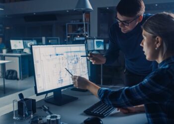 Two workers conversing while working on a project management system at an engineering firm