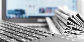 A series of newspapers by a digital or media publication open on a laptop