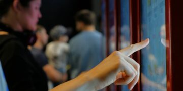 A woman's hand reaching to touch the display of a digital sign at a store.