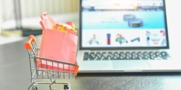 A shopping cart with shopping bags in it in front of a computer symbolising an online eCommerce shopping.