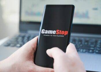 Phone held in front of a laptop, showing the logo of GameStop to the person viewing it.