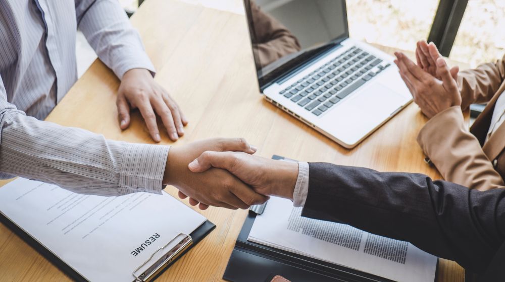 Two people shaking hands after a successful job interview above the resume and a computer.