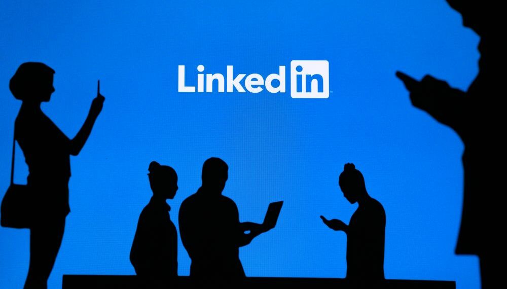 Group of people using Linkedin on their devices with the linkedin logo in the background