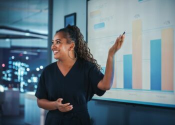 Team member standing up giving hybrid multimedia presentation to external and internal employees