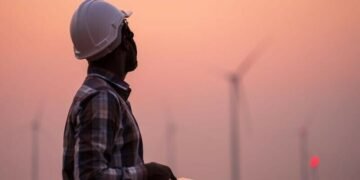 A field worker out by wind turbines with a tablet reviewing their operational capcity