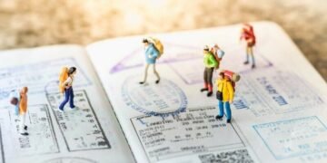 A series of miniature people walking across a passport with lots of residency stamps