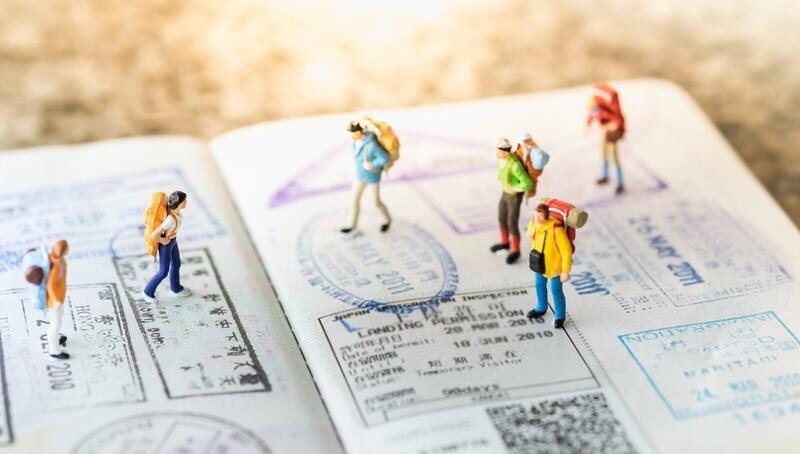 A series of miniature people walking across a passport with lots of residency stamps