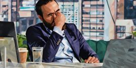 A company director sitting at a desk, holding the bridge of his nose in distress, he's realised he's made serious commercial mistake