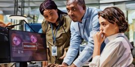 A team of CySec employees gathered around a computer looking stress, as they've just indentified a cyber attack